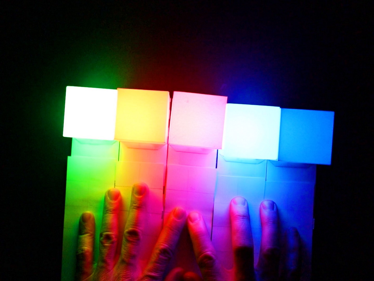 LED-beleuchtete Papier-Würfel in verschiedenen Farben, die durch zwei Hände berührt werden