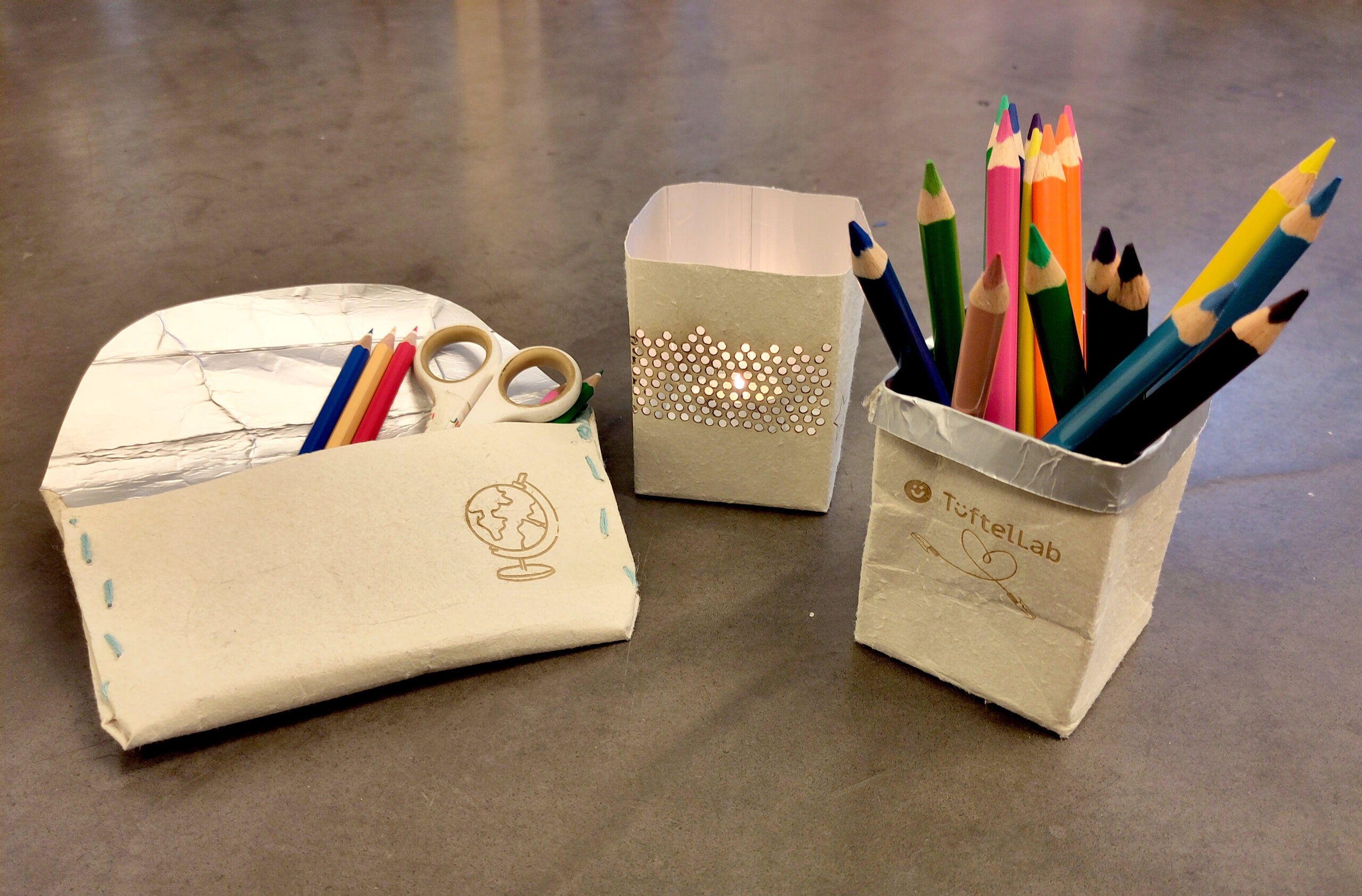 Ein Stifthalter, eine Federtasche und ein Teelicht-Halter aus gebrauchten Tetrapaks, mit lasergravuren verziert.
