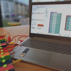 Ein Laptop mit dem geöffneten Programm "Block Music", der über ein Makey Makey mit einem Metallophon verbunden ist.