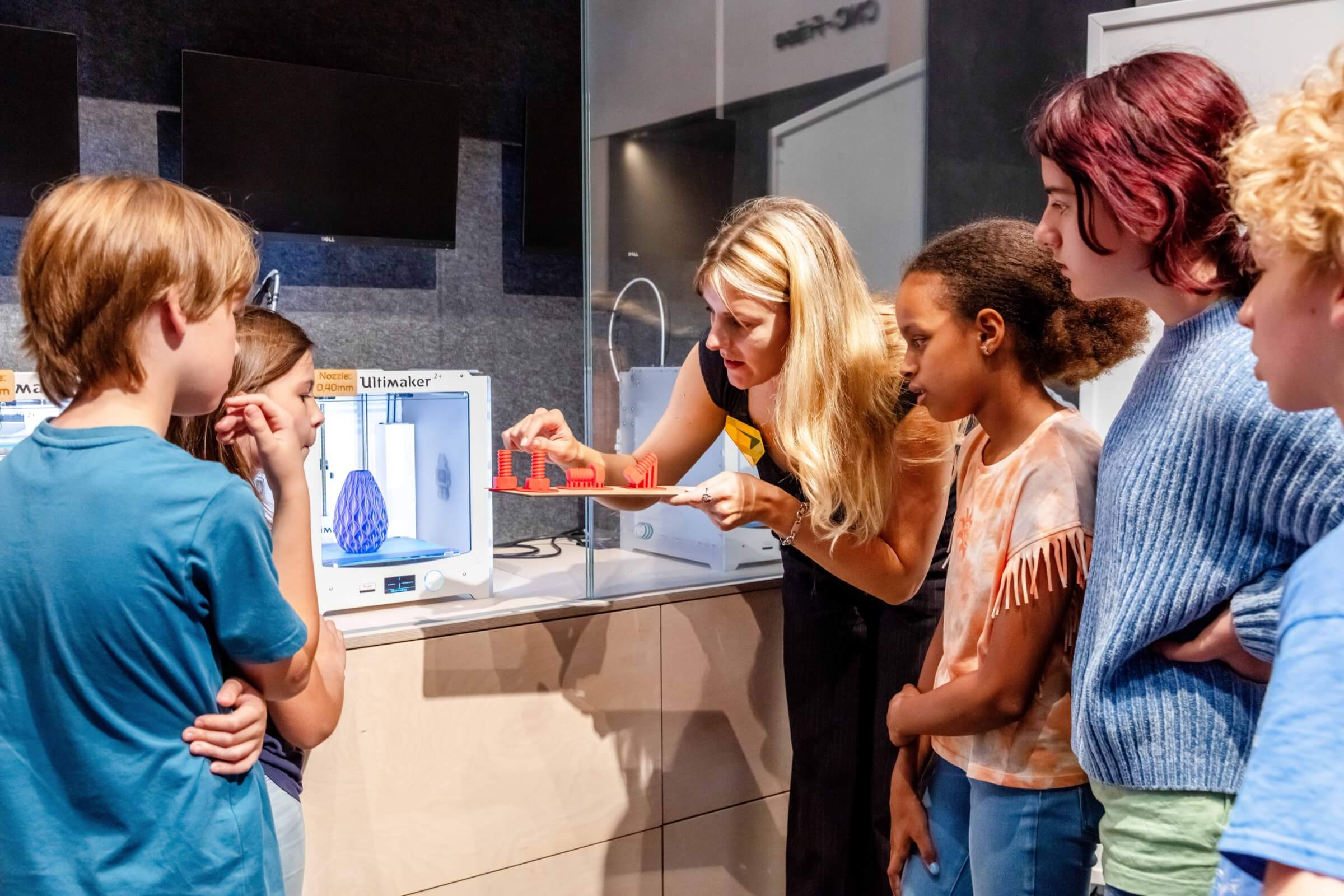Workshopleiterin beschreibt Kindern die Eigenschaften der 3D Druckmodelle
