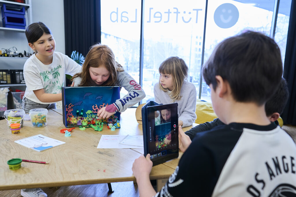 Eine Gruppe Von Kindern Sitzt An Einem Tisch Und Gestaltet Einen Stop Motion Film.