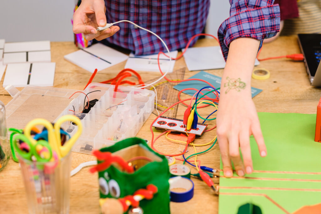 Schulworkshop: “wir brauchen kreatives chaos” - projektleitung lea im interview 3 Kinderhände Tüfteln In Einem Schulworkshop Mit Makey Makey. Überall Liegen Bastelmaterialien Verteilt.